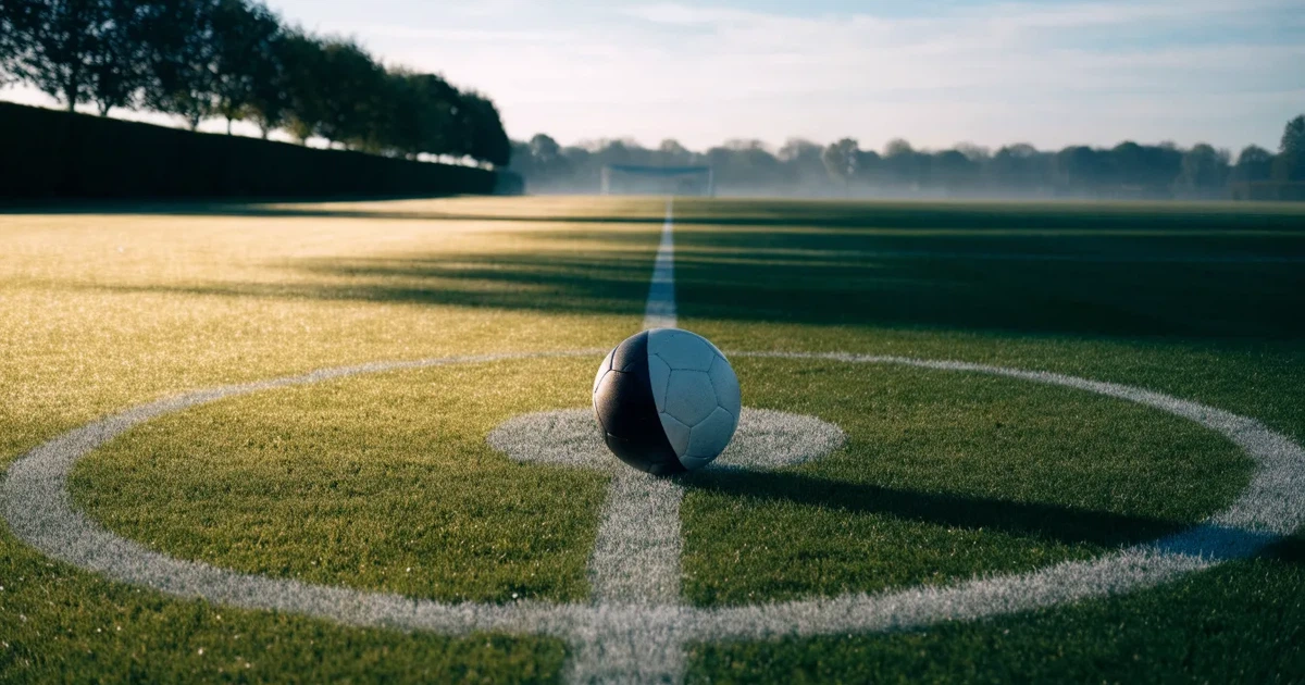 Uma bola de futebol no ponto central de um relvado, à luz da manhã