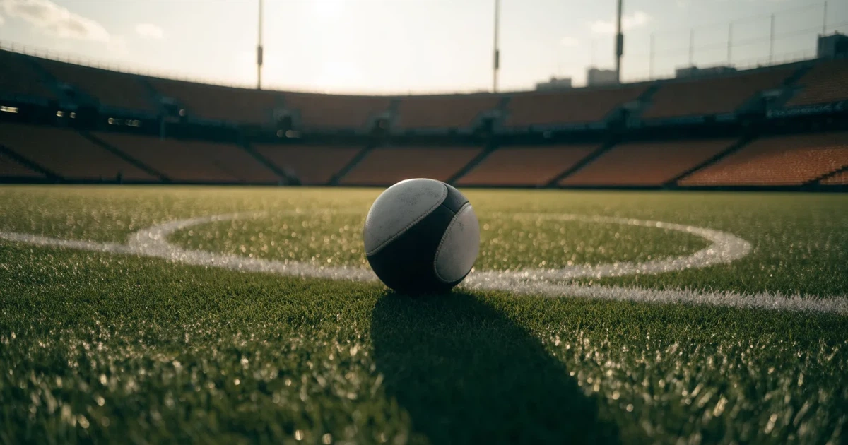 Uma bola de futebol no ponto central de um relvado, à luz da manhã