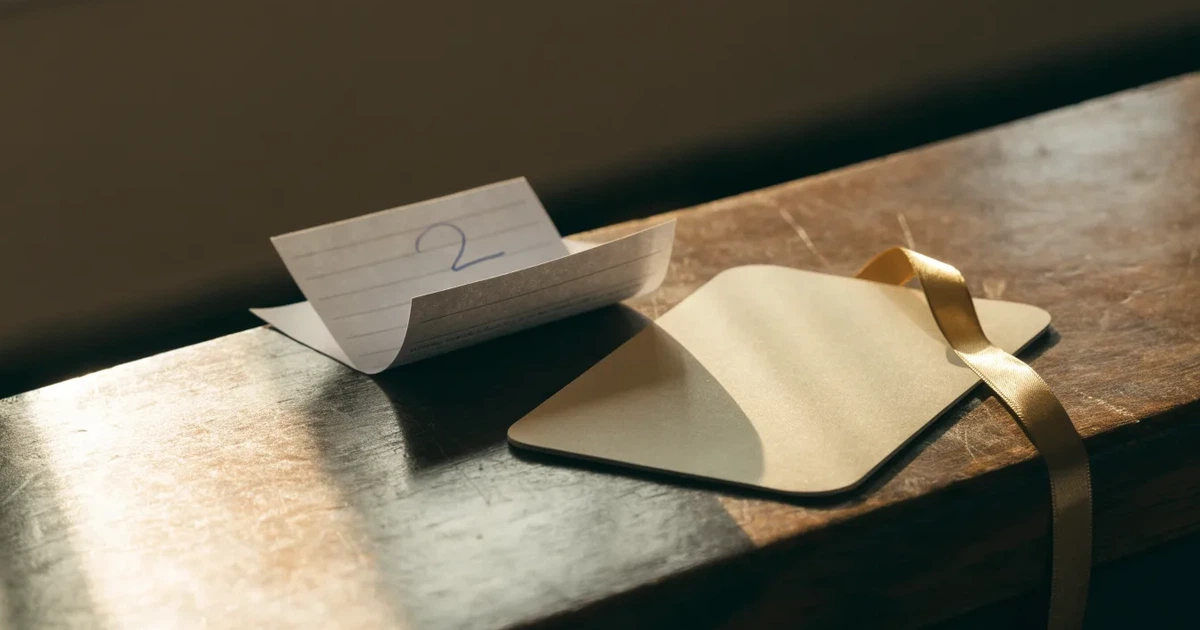 Um cartão de oferta com uma fita dourada ao lado de um talão de apostas numa bancada de madeira